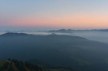 Mystical pastel-coloured alpine landscape after sunset with rocky mountains above clouds and mist. View from the summit of the Gruenten mountain (Allgaeu Alps, Bavaria, Germany).