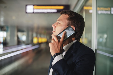 Profile of businessman having conversation on handy. He standing at lobby and seriously looking ahead