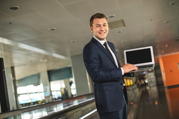 Obraz premium Pasa w górę portret blithesome biznesmen trzymając laptopa i patrząc na kamery z szerokim uśmiechem
