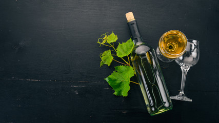 A bottle of white wine with glasses and grapes. Leaves of grapes. Top view. On a black wooden background. Free space for text.