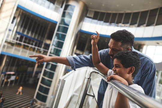 Cheerful Hindu boy standing near handrail with his father who is showing him the airport