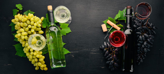 Set of red and white wine in bottles and glasses. Grape. On a black wooden background. Free space for text. Top view.