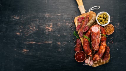 Sausage Fuet, salami, paperboard on the kitchen board. On a black background. Top view. Free space...