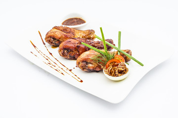 Honey chicken legs with onion, tomatoes, green and bbq sauce on white plate