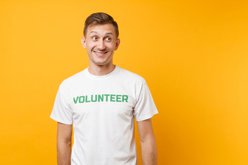 Portrait of happy smiling satisfied young man in white t-shirt with written inscription green title volunteer isolated on yellow background. Voluntary free assistance help, charity grace work concept.