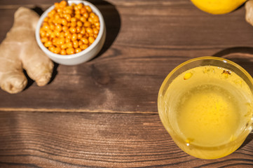 Sea buckthorn tea on a dark wooden textural background. Sea buckthorn, lemon, ginger, books in the background, the concept of warmth, comfort and health in the autumn