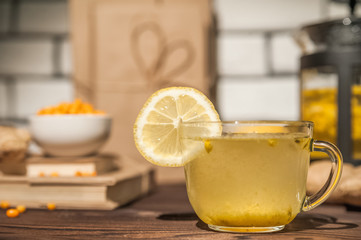 Sea buckthorn tea on a dark wooden textural background. Sea buckthorn, lemon, ginger, books in the background, the concept of warmth, comfort and health in the autumn