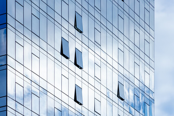 Modern office building with opened windows and reflecting clouds in glass facade