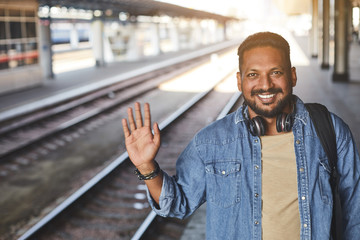 Waist up of a joyful hindu man showing farewall while standing on the railway platform