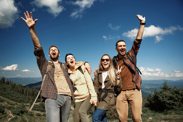 Waist up portrait of joyful two couples hiking in highland. They standing and embracing while having fun together