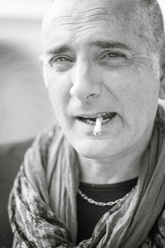A 50y man is smoking a cigarette. Black and white. The fan coil of an air-conditioner is on the background.