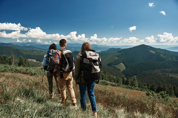 Two women and man carrying rucksacks while tour in highland. They standing on top and looking at...