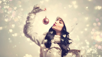 Woman holding Christmas bauble on shiny hearts background