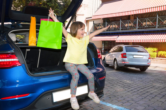 The little girl with colourful bags for purchases, sits in a car luggage carrier.