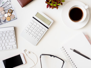 top view of accounting concept with keyboard, smartphone, notebook, coffee cup, calculator and money on white table background.