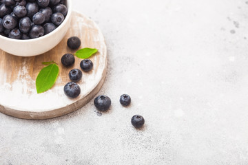 Fresh raw organic blueberries with leaf in white china bowl on stone kitchen background. Space for text