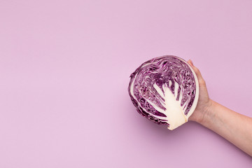 Hand holding purple cabbage half on violet background