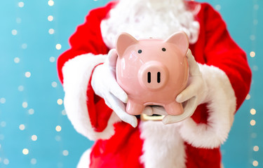 Santa holding a piggy bank on a shiny light blue background