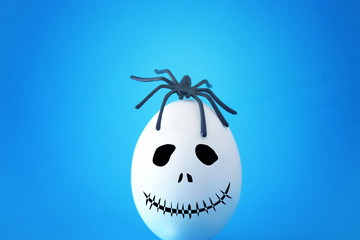 minimal and funny Halloween holiday concept. White egg with scary cute face and spider on top.