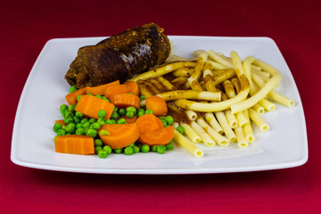 Roulade vom Rind mit Nudeln, Erbsen, Möhren und soße auf einem Teller