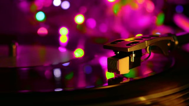 Vinyl recrod played spinning disc. Needle drops on the disc. Cyan light bulbs.