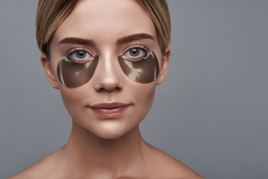 Close up of pretty relaxed woman standing alone and looking calm while having eye patches on her skin