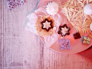 Christmas and New Year decorative composition of handmade decor, snowflakes, hearts, cookies and chocolate on a pink dish on a wooden table, red lighting, concept of seasonal holidays, home comfort, t