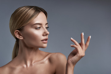 Looking at fingers. Thoughtful young woman standing against the grey background with naked...