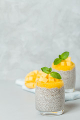 Chia seeds pudding with mango puree in beautiful glasses with green mint leaves and cut fresh ripe tropical fruit.