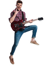 excited guitarist jumping and making rock on sign during concert