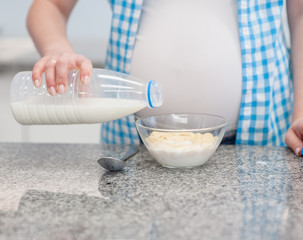close up pregnant woman pours milk into a dry breakfast