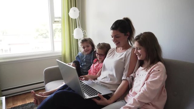 mother and daughters on sofa at home using laptop