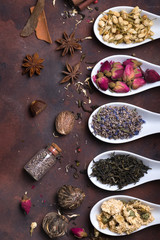 Ceramic spoons with dried herbs, flower buds and tea leaves with spices over stone background, top view,
