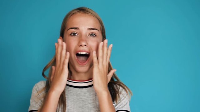 Beautiful happy surprised girl with positive emotions over blue background. Portrait of cute surprised and shocked teen girl. Happy, shocked, surprised and smiling woman standing isolated over blue
