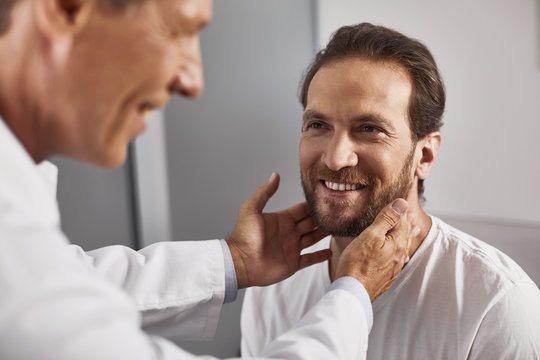Smiling doctor testing lymph nodes to checking their size and absence of inflammation of male patient