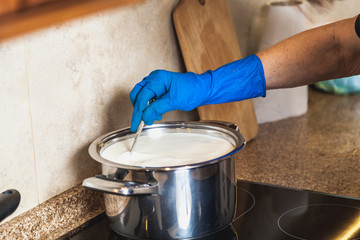 Blue glove hand stirring milk in pan