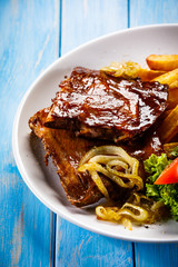 Grilled ribs, French fries and vegetables on wooden background