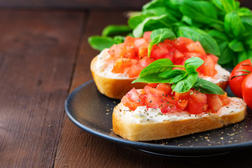 Traditional toasted Italian tomato bruschetta with spice and basil on dark wooden board