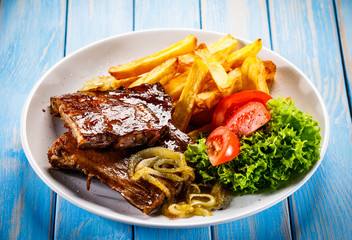 Grilled ribs, French fries and vegetables on wooden background
