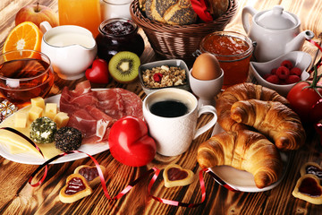 breakfast on table with bread buns, croissants, coffe and juice on valentines day.