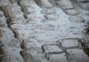 RAIN DROPS SPLASHING IN PUDDLE ON COBBLED STREET