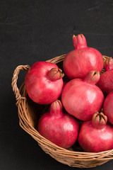 Ripe red pomegranates in wicker basket closeup photography on black background.