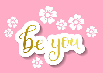 Modern calligraphy lettering of Be you in golden in paper cut style on pink background with white flowers for decoration, poster, sticker, postcard, motivation, slogan, motto, greeting card