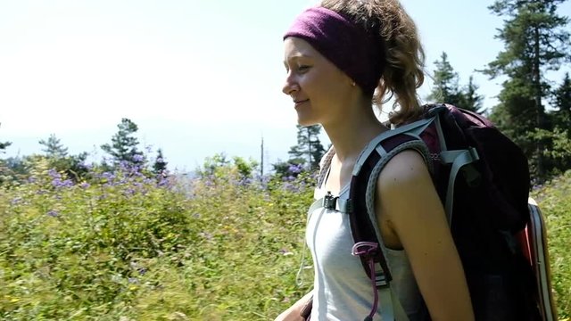 Happy woman tourist in a hike goes with a backpack and smiles, slow motion, camera movement