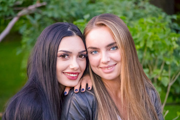 Girlfriend girls in the Park on the background of green bushes and lawn. Two girls in the park