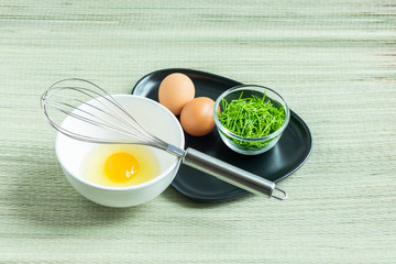 Acacia Pennata (Climbing Wattle) in small glass bowl with two eggs and a whisk on black plate and one raw egg in white bowl.