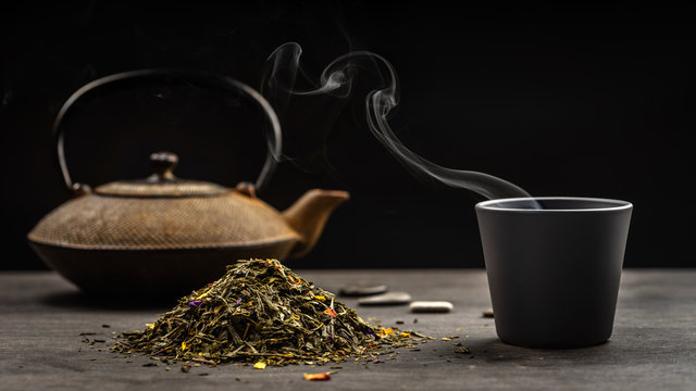 un tas de feuilles de thé avec une tasse et une théière en fond