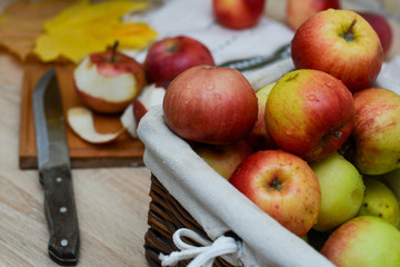 basket of apples, some apples are on the table, a cutting board and a knife.