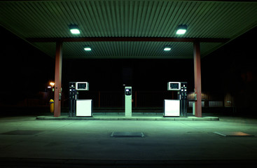 Dunkle, grün beleuchtete Tankstelle bei Nacht im Industriegebiet