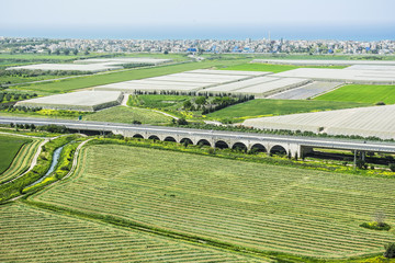 Agriculture scenic view of green fields and greenhouses, road, bridge, blue sea and sky in Israel